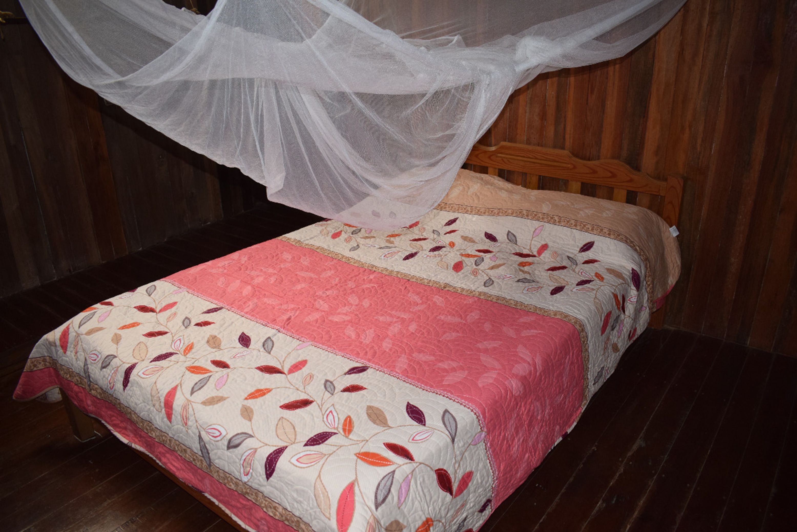 A bed with a floral-patterned bedspread and a mosquito net above it.