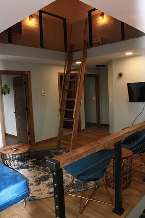Un ambiente abitativo in stile loft con una scala in legno, una televisione montata a parete e un divano blu.