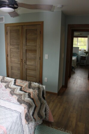 A bedroom with a large wooden wardrobe, a bed with a patterned blanket, and a hallway leading to another room.