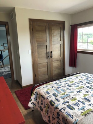 A bedroom with a bed, a wardrobe, a window with curtains, and a red rug.