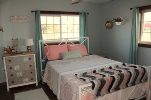 A bedroom with a bed, dresser, and a window with curtains.