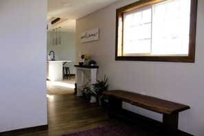 A hallway with a wooden bench, a welcome sign, and a window with blinds.