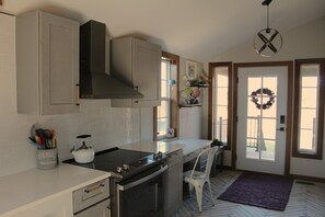 A kitchen with a stove, oven, and cabinets. There is a white chair and a purple rug. - 1900 FARMHOUSE (Wausau)