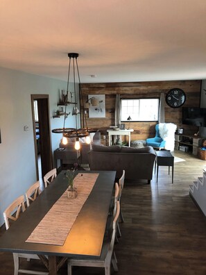 A modern living space with a dining area, a sofa, a TV, and a clock on the wall. - 1900 FARMHOUSE (Wausau)