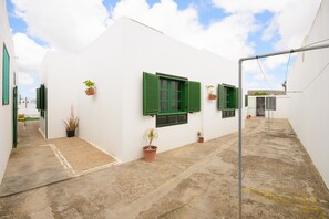A narrow alleyway with white walls and green shutters, potted plants, and a concrete ground.