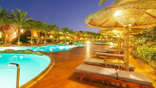 A pool area with lounge chairs and umbrellas, surrounded by palm trees and a night sky. - Floriana Dream Lagoon (Marsa Alam)