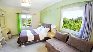 A bedroom with a bed, a sofa, a window with curtains, and a view of greenery. - Vliho Bay Suites And Apartments (Lefkada)