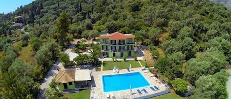 Una amplia villa con piscina, rodeada de exuberante vegetación y montañas al fondo.