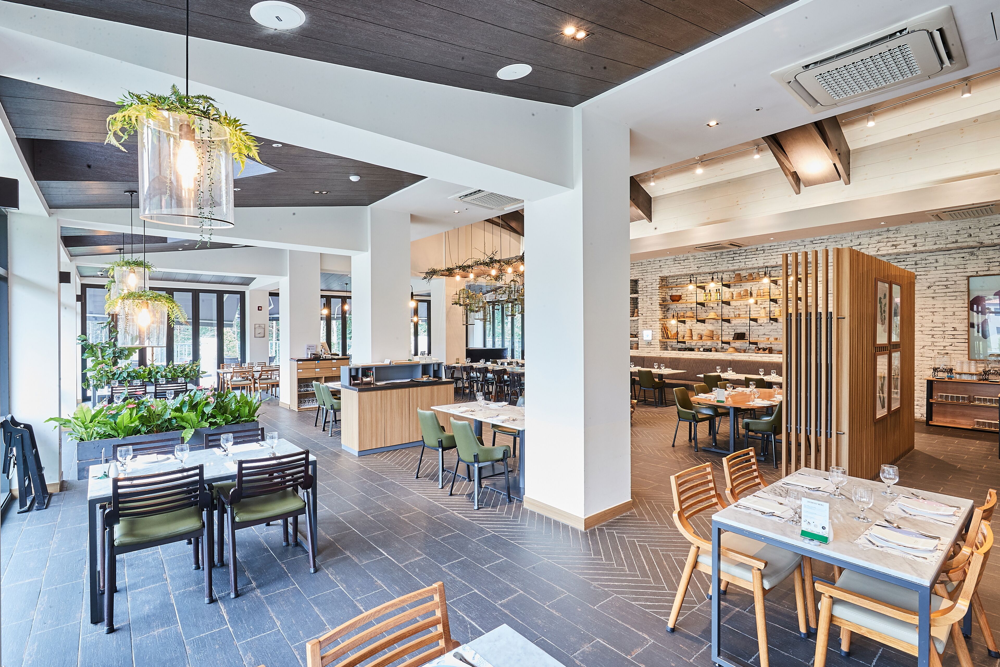 A modern restaurant with high ceilings, exposed brick walls, and a variety of seating arrangements including tables and booths.