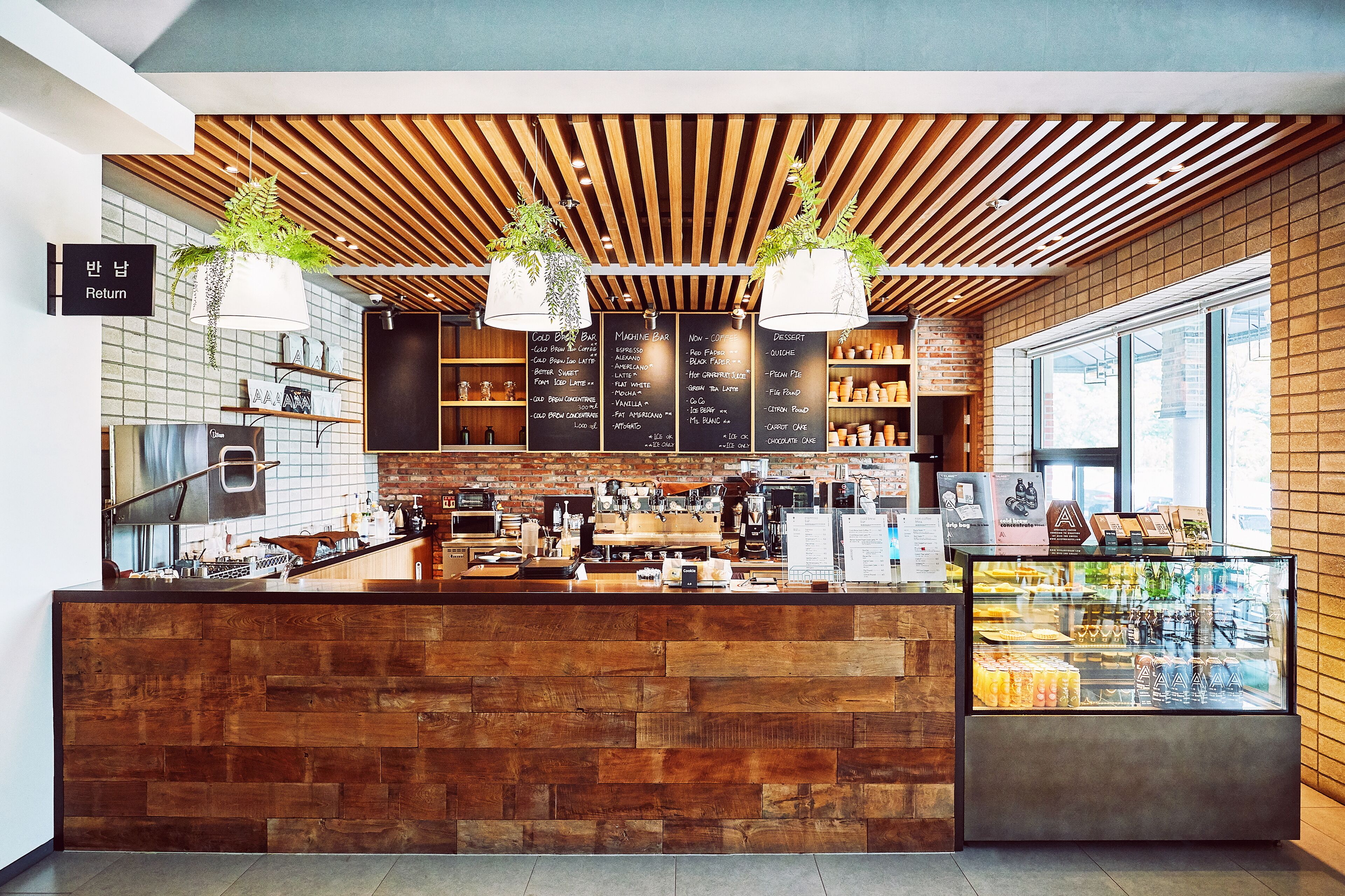 Un café moderne avec un comptoir en bois, des plantes suspendues et un tableau affichant le menu.