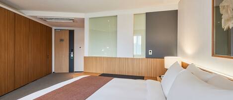 Ein modernes Hotelzimmer mit einem großen Bett, einem Holzschrank, einem Nachttisch mit Lampe und einem großen Spiegel.