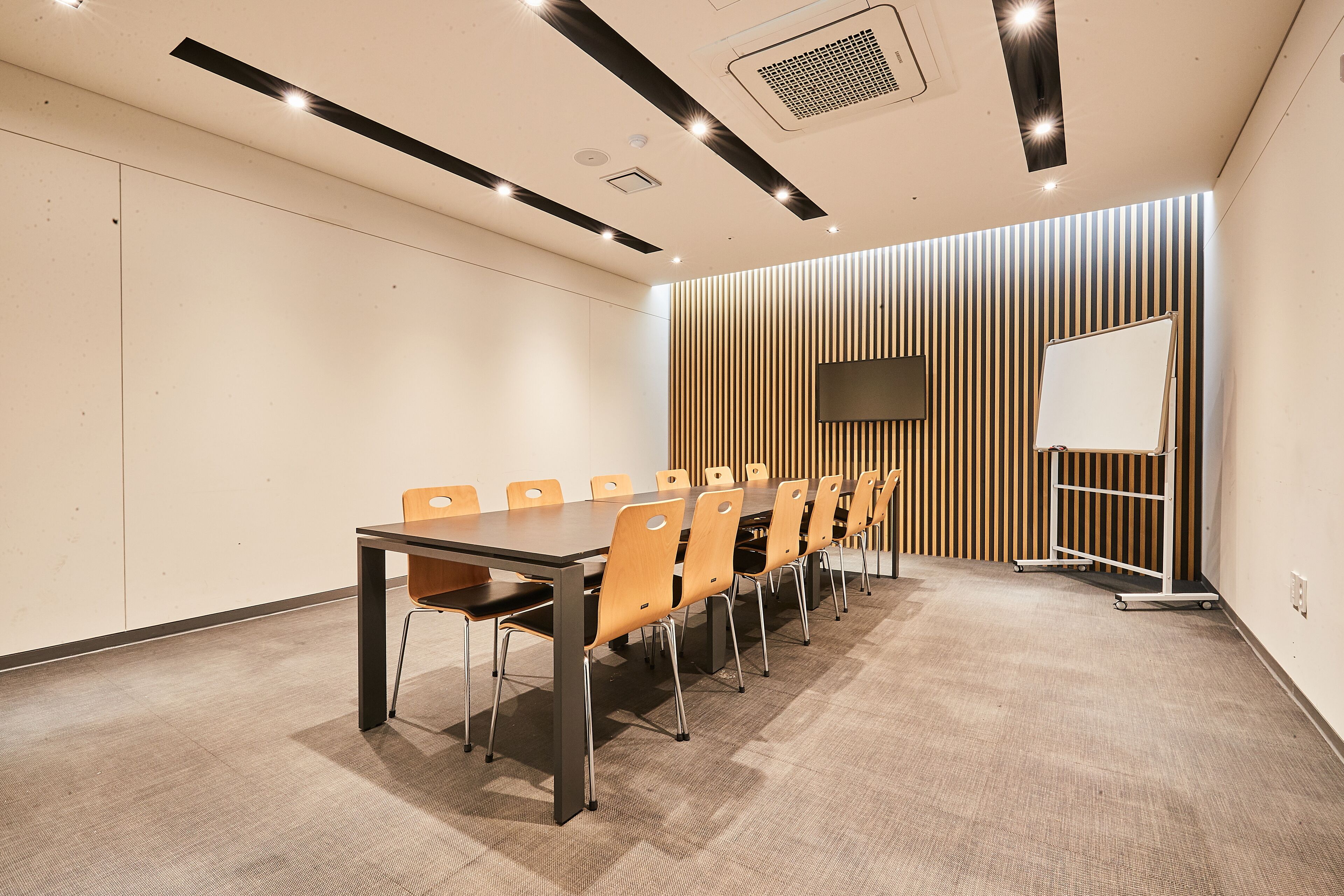 A conference room with a long table, chairs, a whiteboard, and a TV screen.