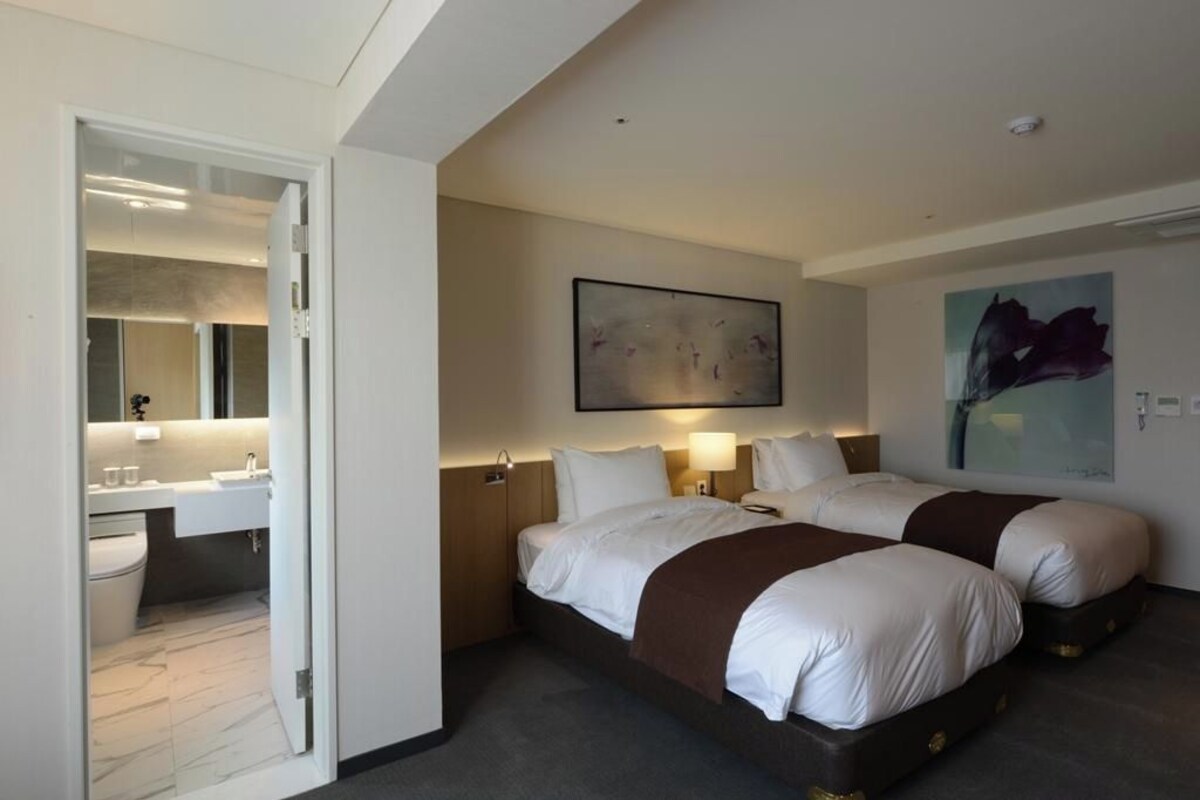 A hotel room with two beds, a bathroom, and a large abstract painting on the wall.