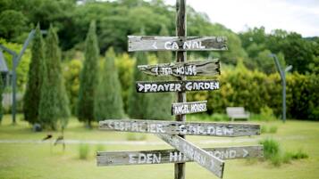A wooden signpost with multiple directional arrows pointing to various destinations such as "Canal," "Tea House," "Prayer Garden," and "Angel House."