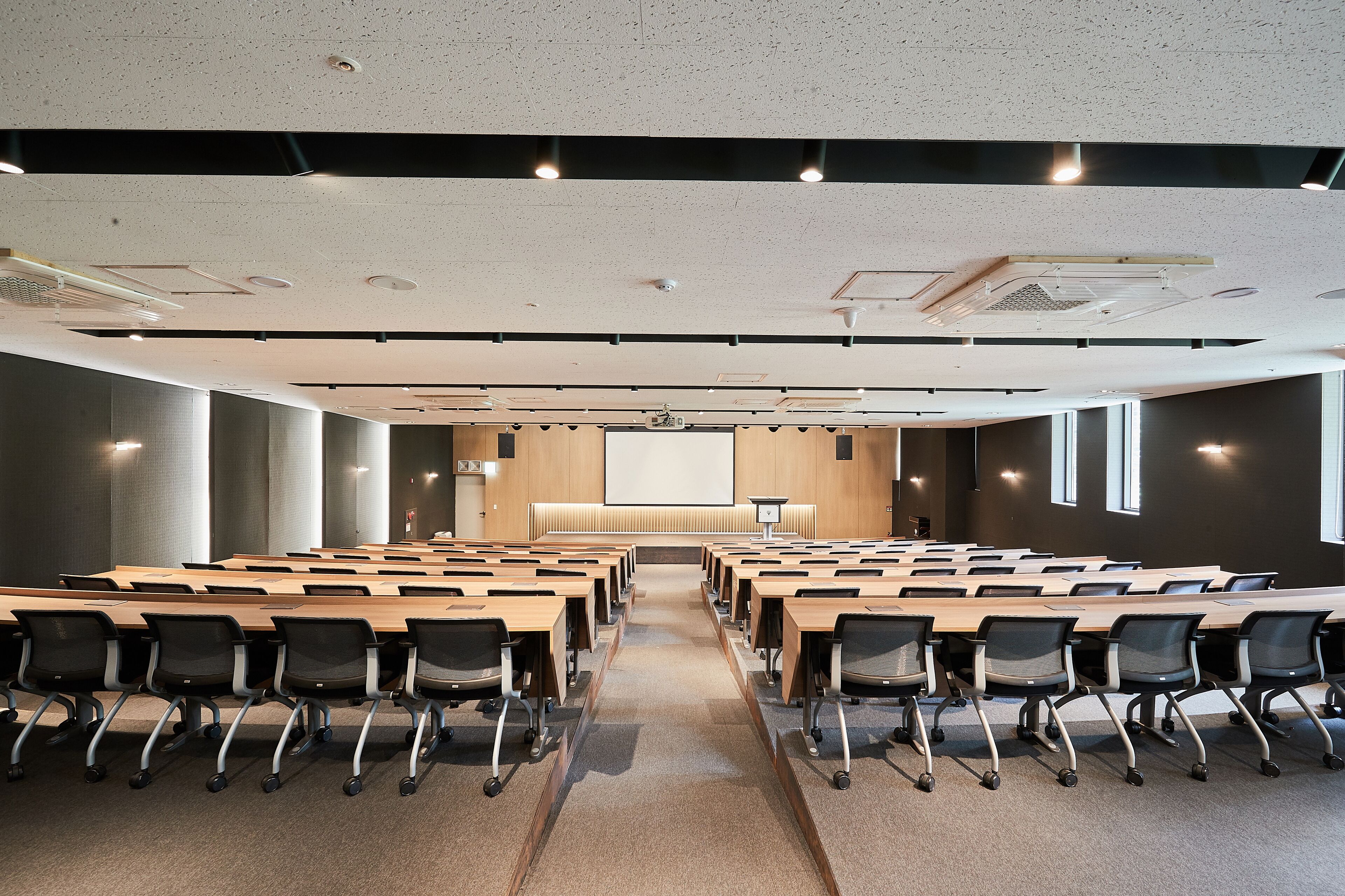 A conference room with long tables and chairs, a projector screen, and a large window.