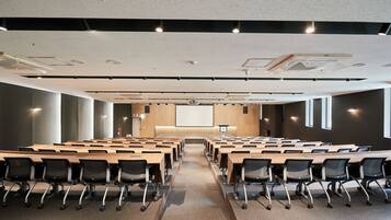 A conference room with long tables and chairs, a projector screen, and a large window.