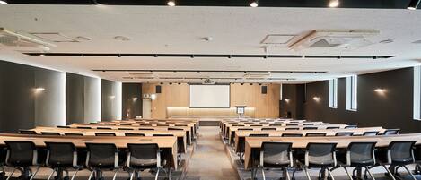 A conference room with long tables and chairs, a projector screen, and a large window.