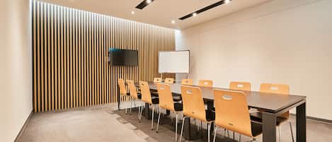 A conference room with a long table, multiple chairs, a flat-screen TV, and a whiteboard.