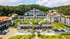 A hotel with multiple buildings, a parking area, and a surrounding forested landscape. - Eden Paradise Hotel (Icheon)