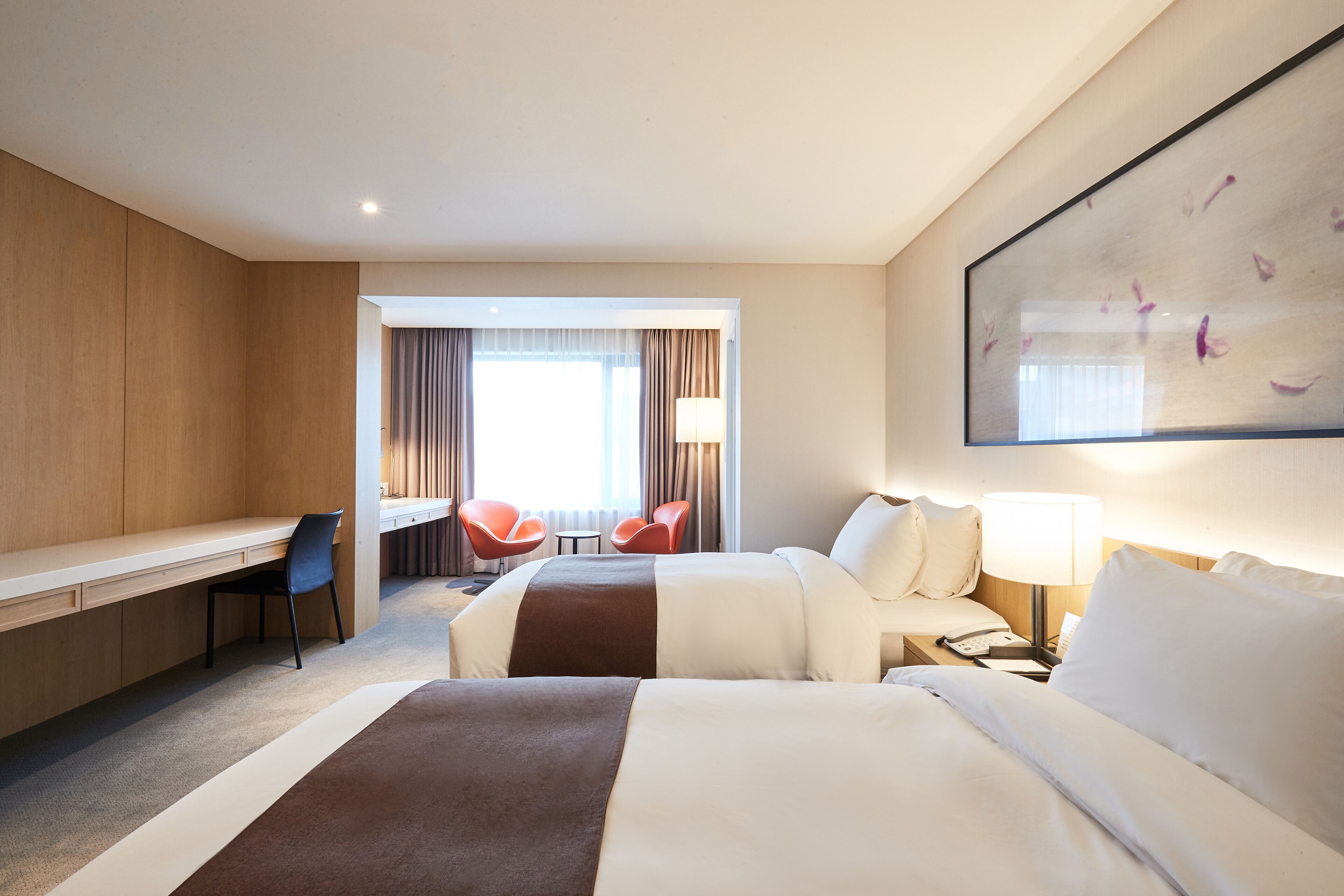 Une chambre d’hôtel avec un bureau, deux lits, une chaise et un tableau au mur.