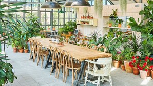 A spacious greenhouse with a wooden table and chairs, surrounded by potted plants and hanging greenery. - Eden Paradise Hotel (Icheon)