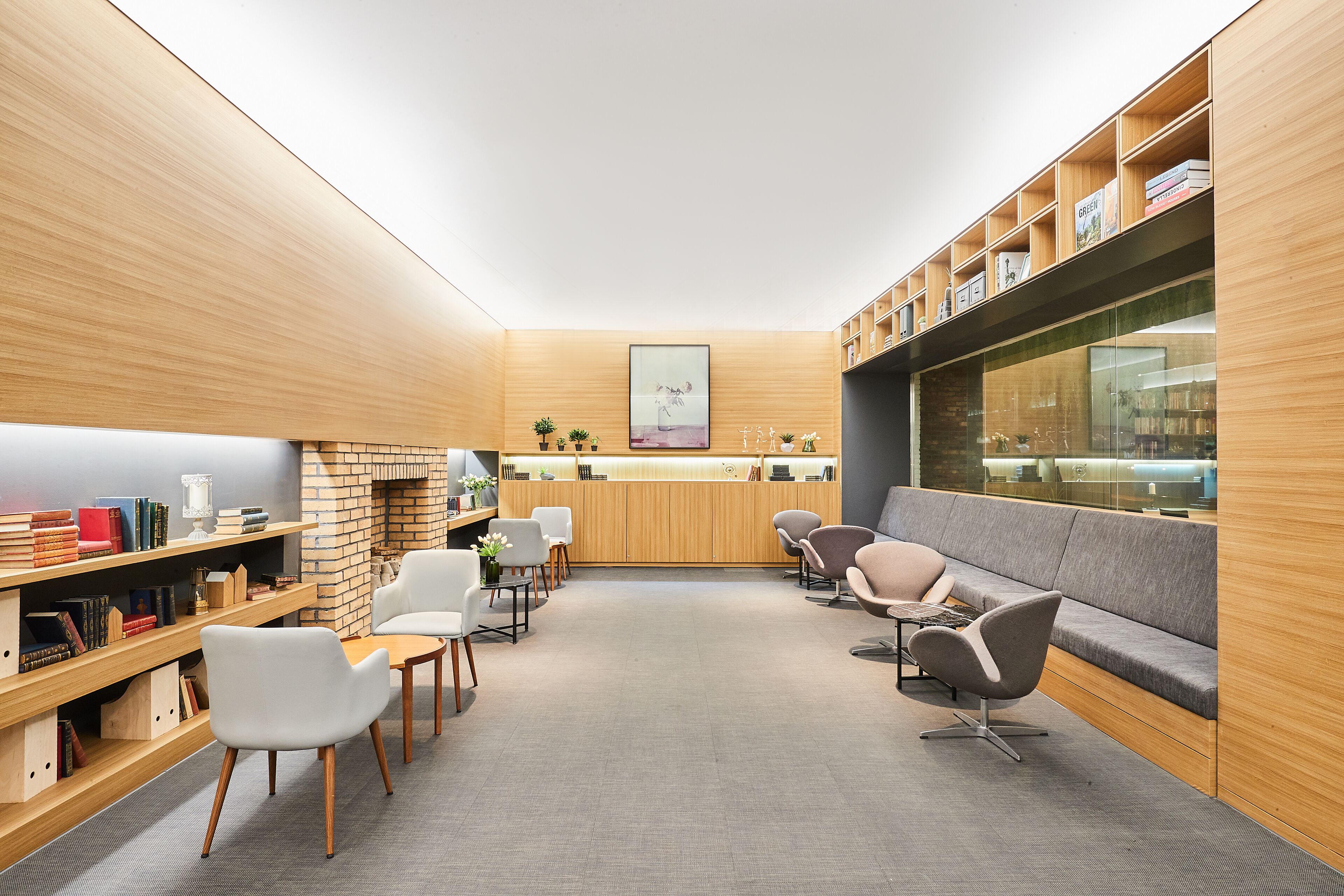 A modern library with wooden bookshelves, seating areas, and a fireplace.