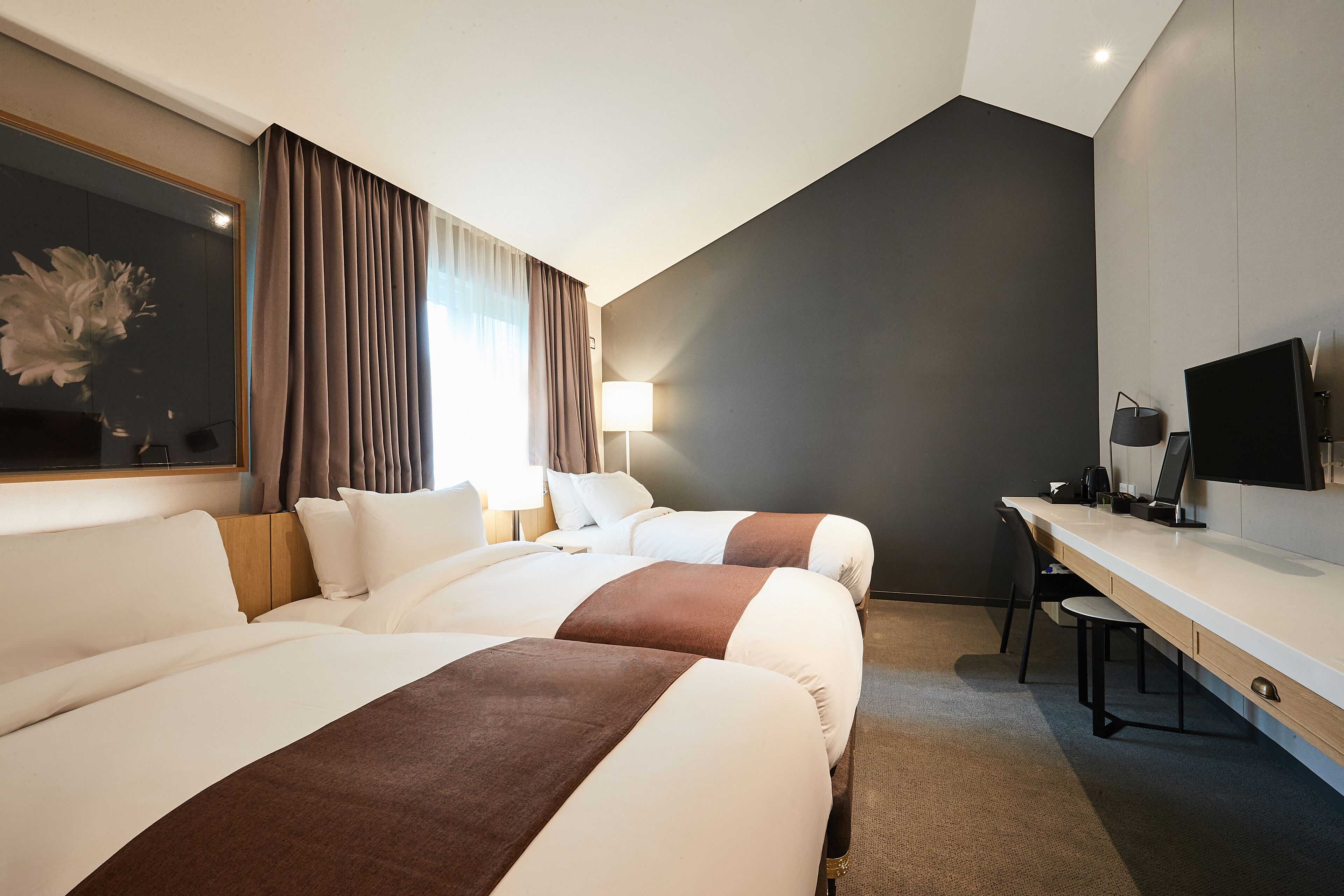 Habitación de hotel con dos camas, un escritorio, una silla, un televisor y una lámpara.