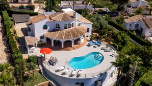Une grande maison avec une piscine, plusieurs chaises longues et un parasol rouge.