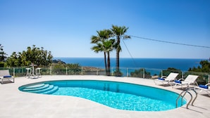 Une piscine à l’eau d’un bleu cristallin, entourée de chaises longues blanches et d’un palmier.