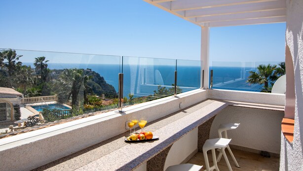 Un balcon avec une piscine, une table garnie de fruits et de boissons, et une vue sur l’océan.