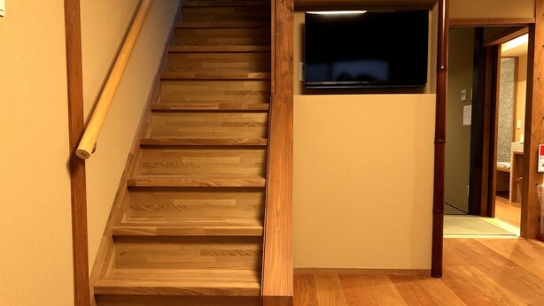 A wooden staircase with a handrail, leading to a landing with a flat surface and a dark object on top. - Mokuren (Kyoto)