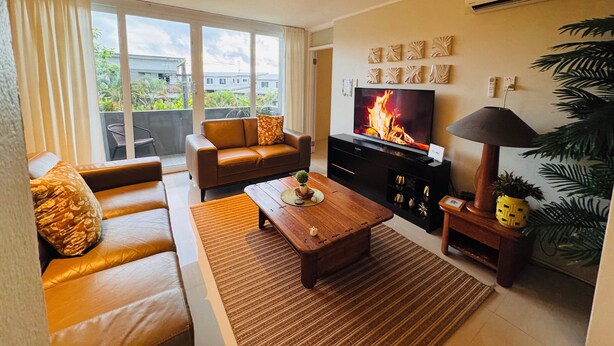 A living room with a sofa, a coffee table, a TV, and a plant. - Kidsfirst Apartment 3 (Suva)