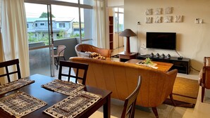A modern living room with a sofa, TV, and dining area with placemats. - Kidsfirst Apartment 3 (Suva)