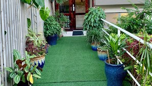 A narrow pathway leading to a building entrance with a wooden door, surrounded by potted plants and a white fence. - Kidsfirst Apartment 3 (Suva)