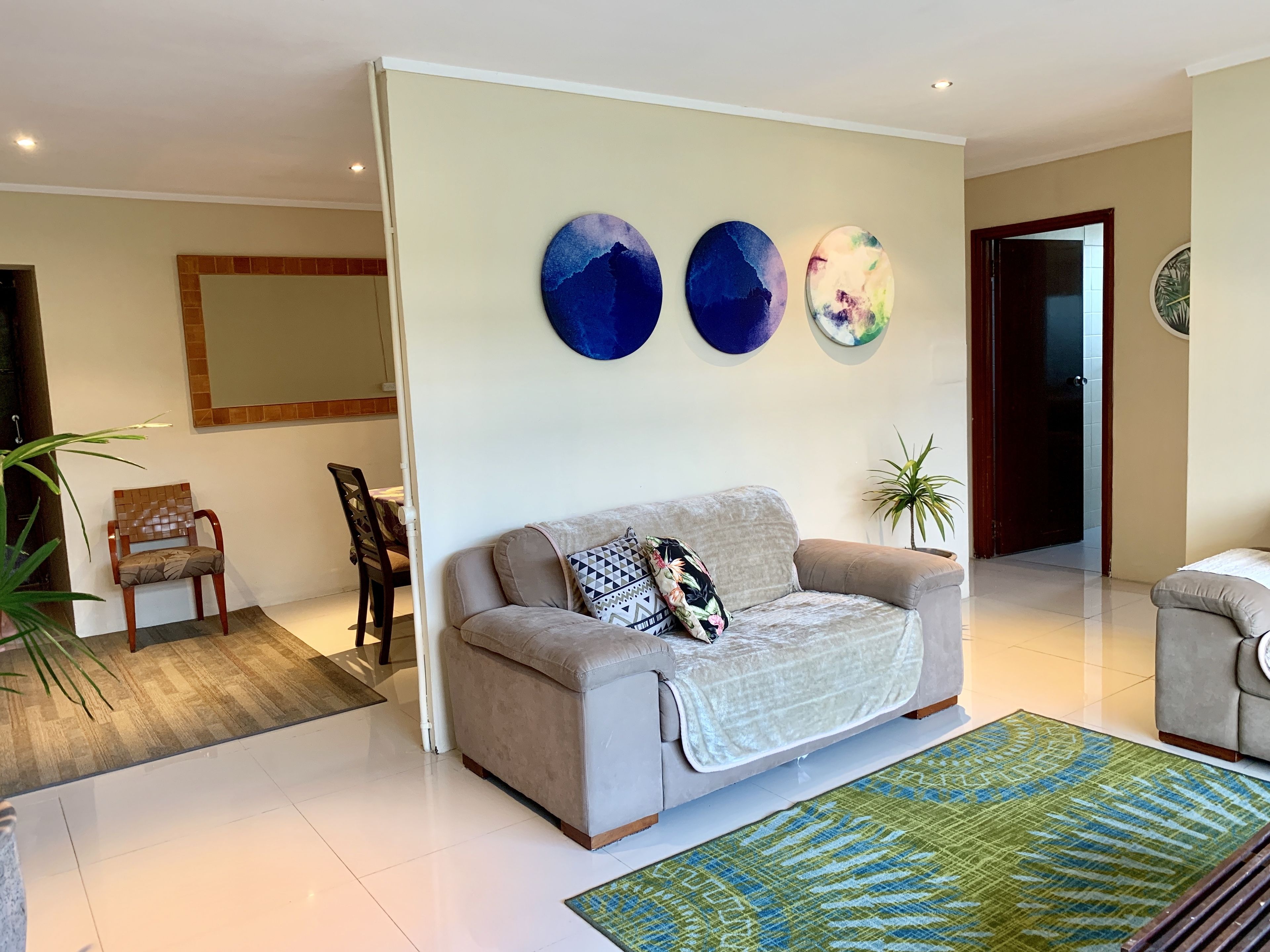 A modern living room with a sofa, a coffee table, and a large rug. There are three abstract wall art pieces above the sofa.