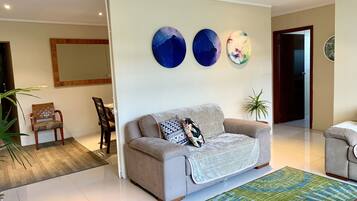 A modern living room with a sofa, a coffee table, and a large rug. There are three abstract wall art pieces above the sofa.