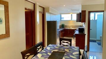 A dining area with a table set for four, a kitchen with wooden cabinets, and a view of the outside through a window.