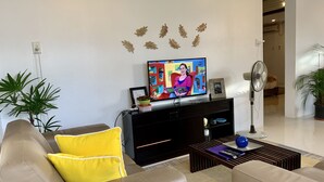 Una sala de estar con un sofá, una mesa de centro, un televisor y un ventilador.