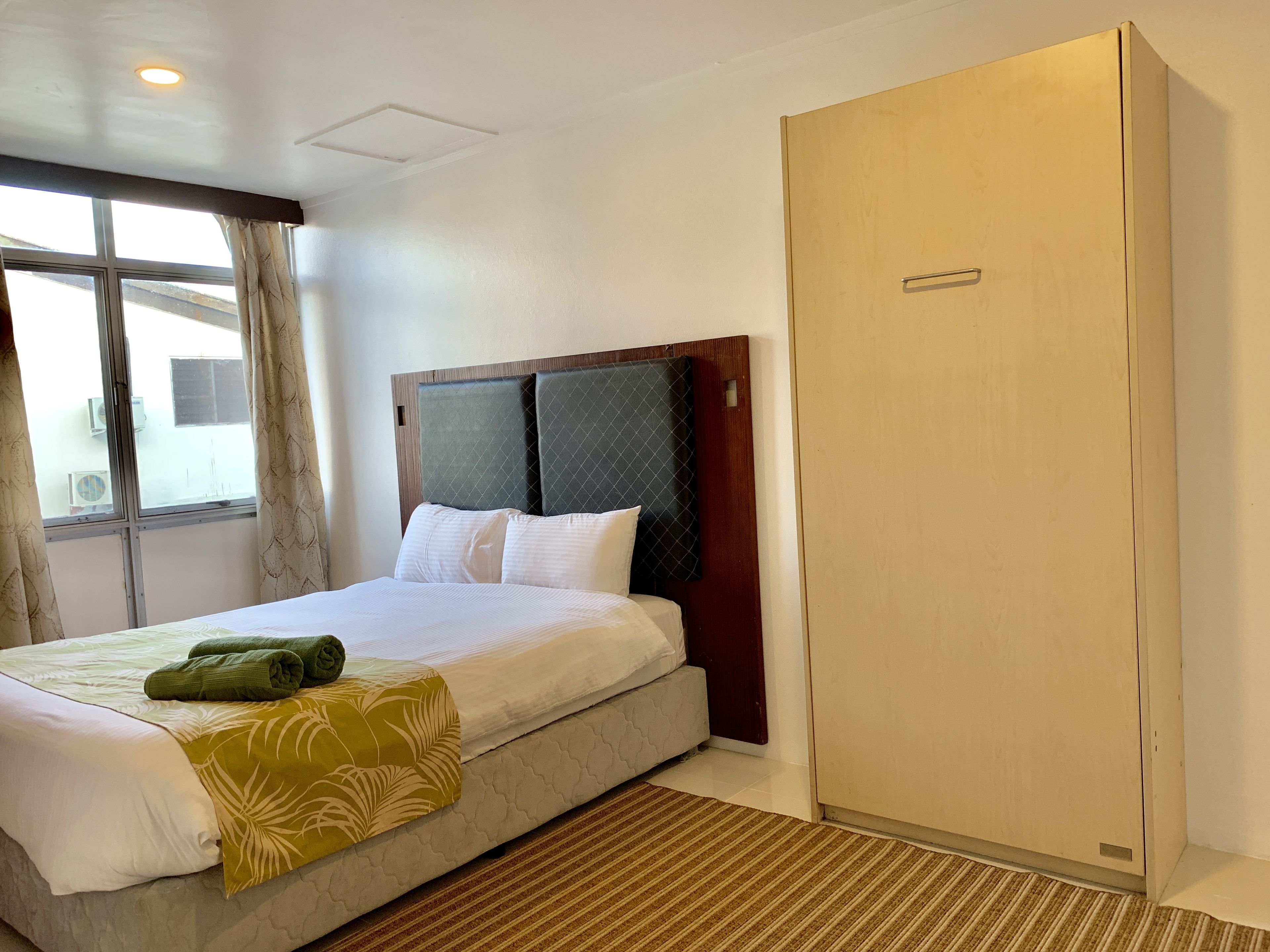 Habitación de hotel con cama, armario, ventana con cortinas y una lámpara en el techo.
