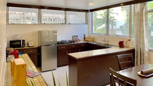 Cocina equipada con refrigerador, microondas, estufa y lavamanos. Se ve follaje a través de la ventana.