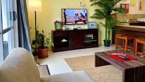 Ein Wohnzimmer mit Fernseher, Sofa, Couchtisch und einer Zimmerpflanze.