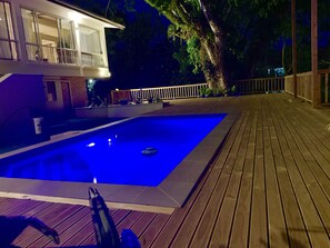 A swimming pool with a wooden deck, a building with a balcony, and a tree in the background. - The Williamson House (Suva)