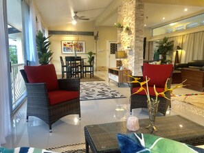 A spacious living area with wicker furniture, red cushions, a glass coffee table, and a decorative vase. - The Williamson House (Suva)