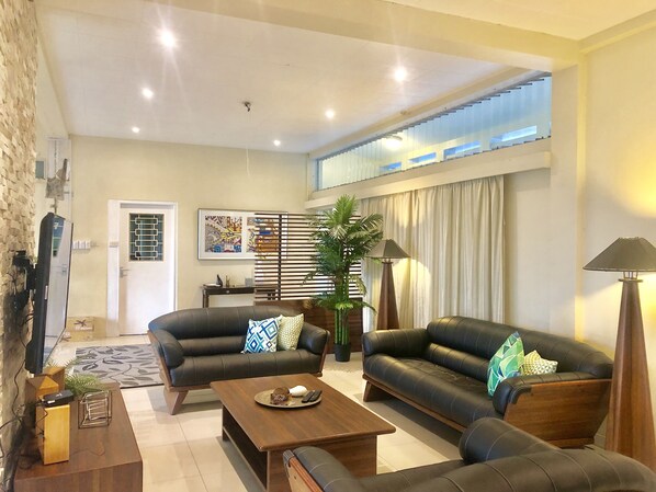A spacious living area with two black leather sofas, a wooden coffee table, and a large potted plant. - The Williamson House (Suva)