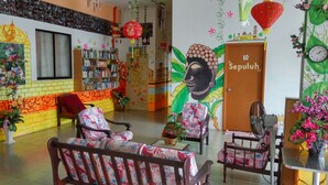 Een kamer met een bank, stoelen, een boekenkast, een muurschildering en een deur met de tekst 'Sepuluh'.