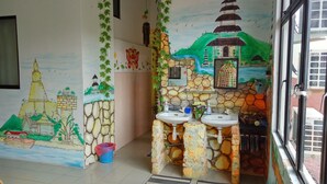 Een badkamer met een muurschildering van een tempel en een pagode, een wastafel met spiegel, en een raam met uitzicht op een gebouw buiten.