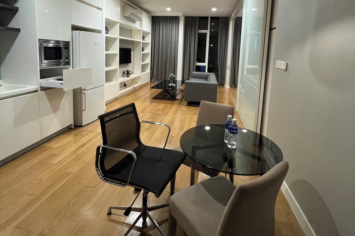 A modern kitchen with white cabinetry, a built-in microwave, and a dining area with a glass table and chairs.