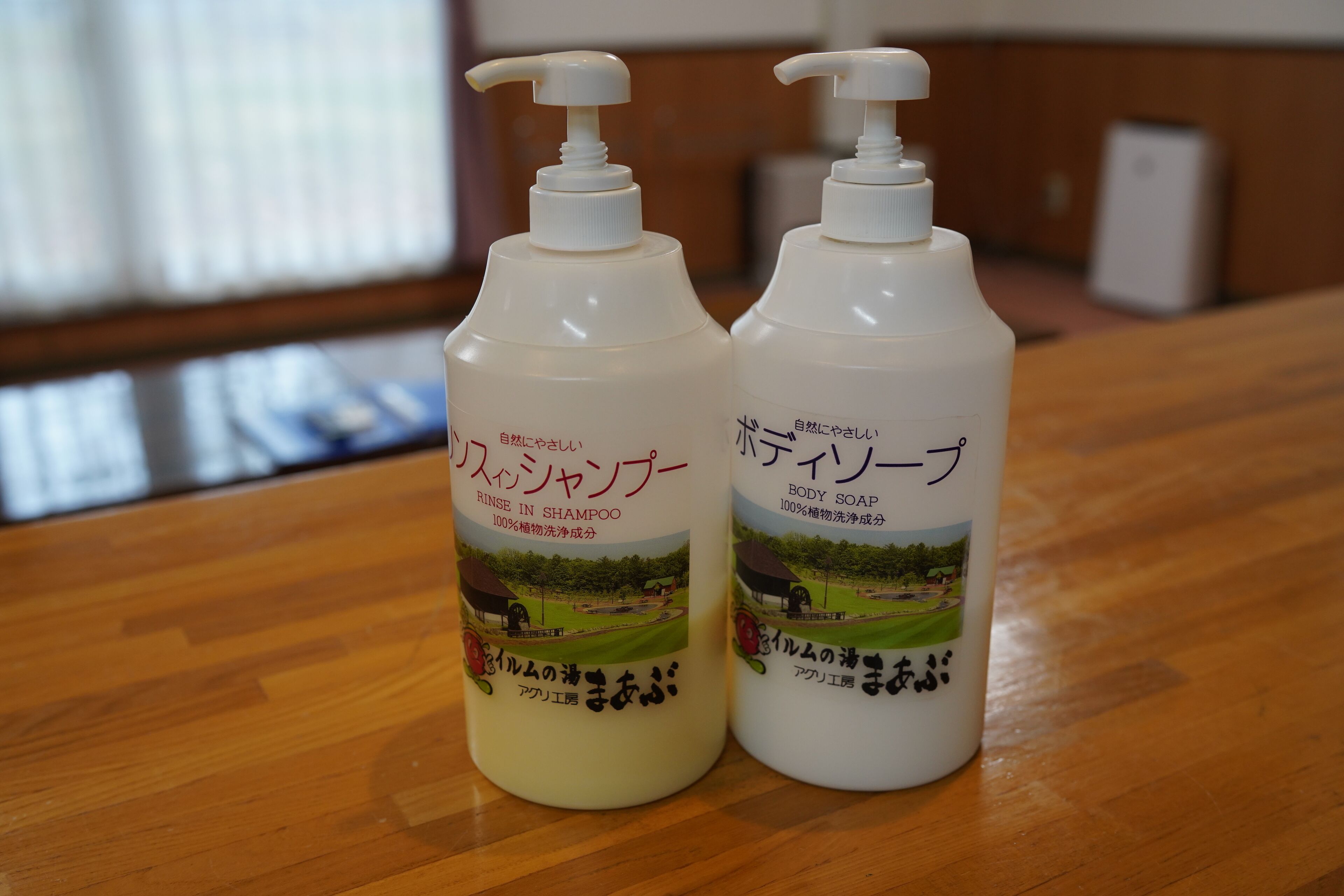Two bottles of body soap and rinse in shampoo on a wooden table.