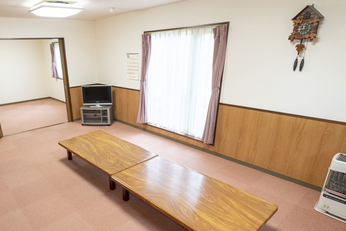 A room with a wooden bench, a television, a clock, and a window with curtains.