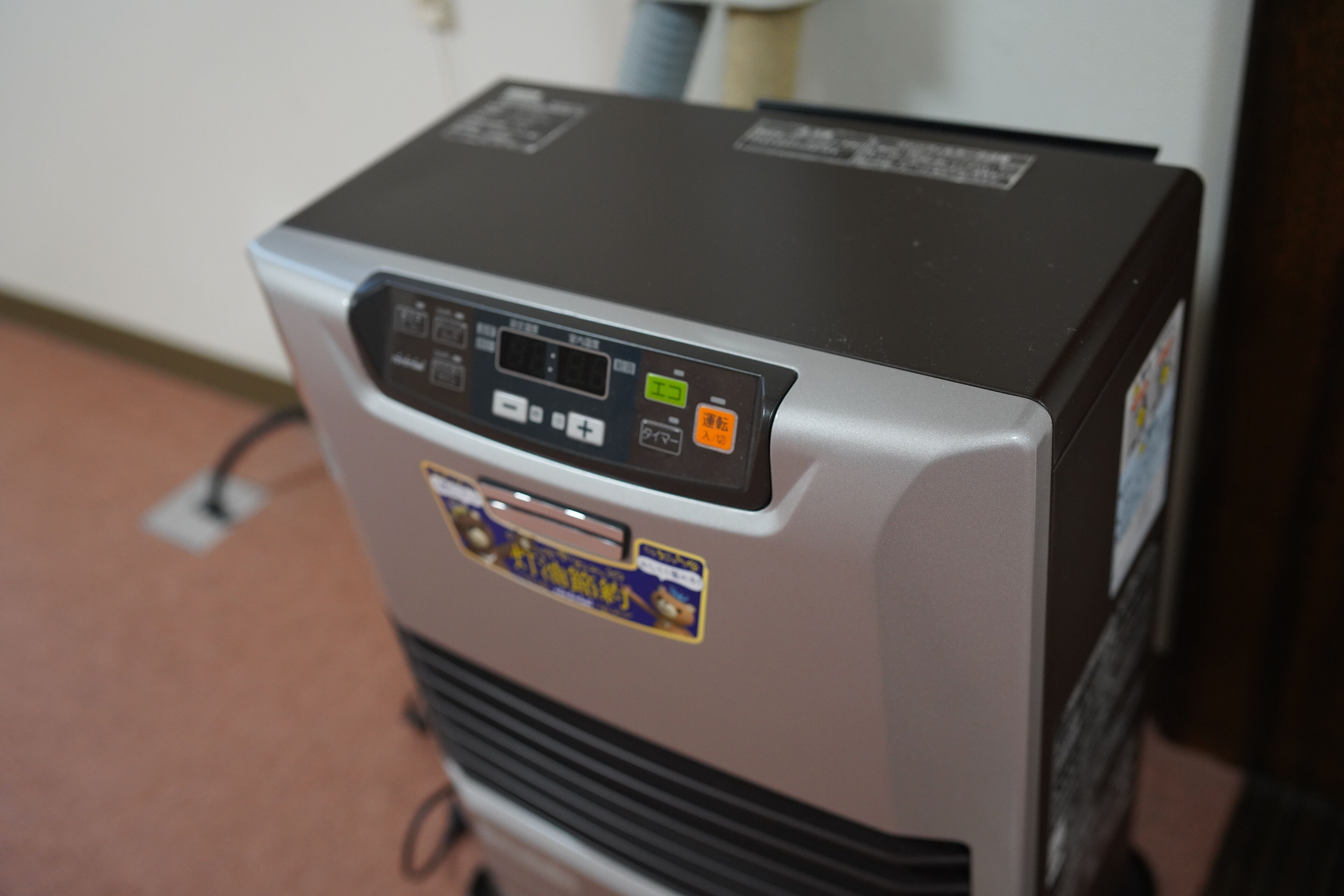 A compact, silver and black refrigerator with a digital control panel, a power cord, and a sticker.